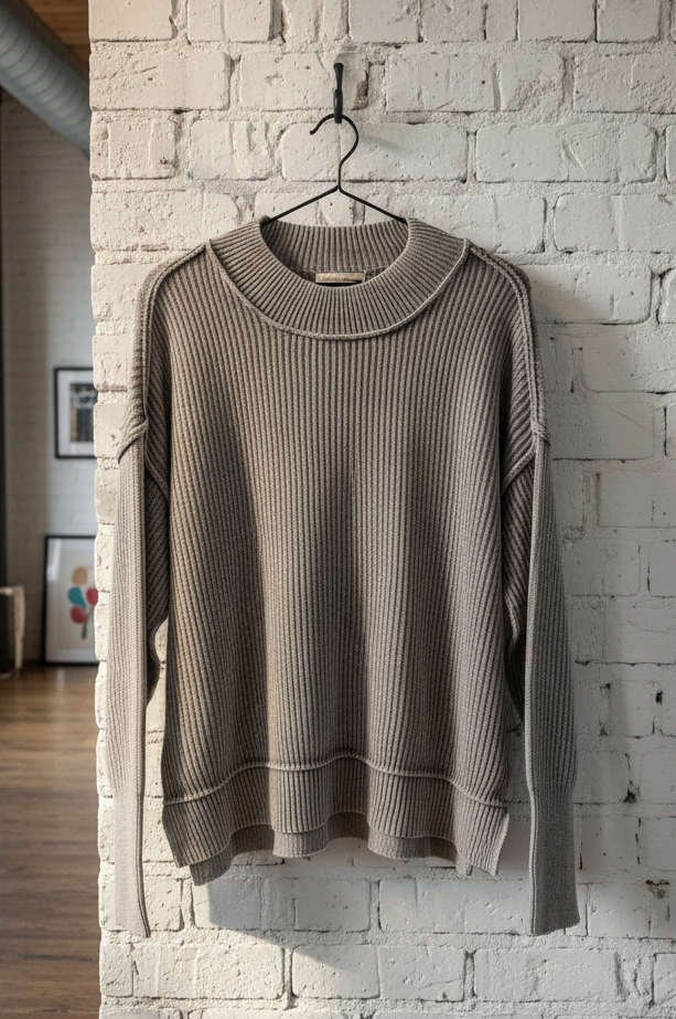 grey sweater hanging on a hook against a white brick wall.