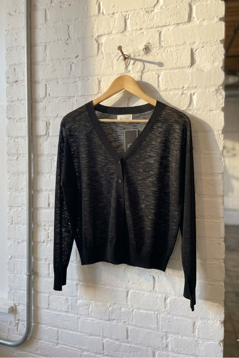 Black cardigan on a hanger against a white brick wall