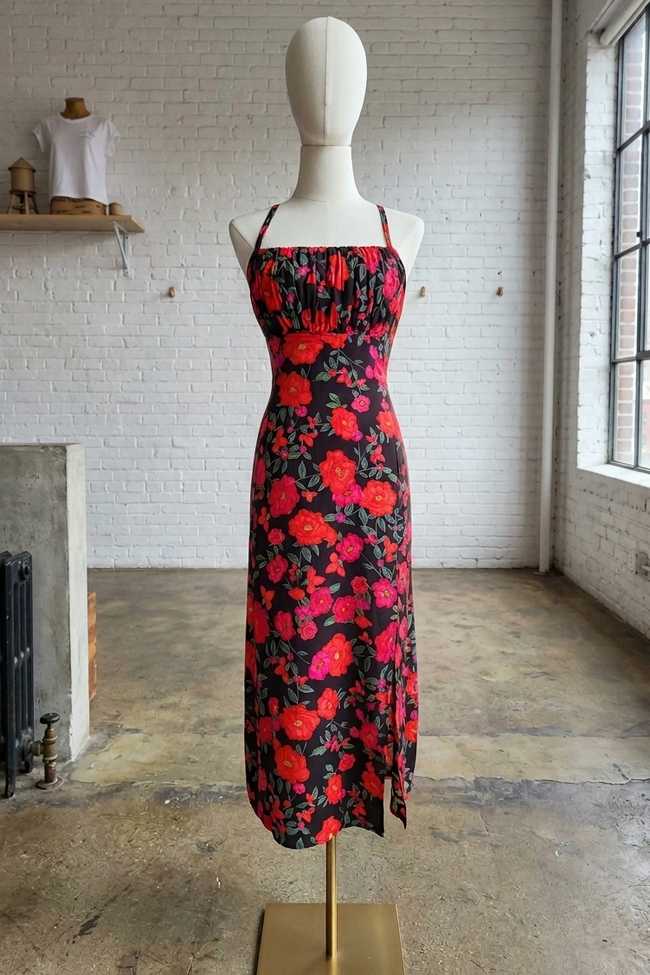 Mannequin wearing a red and black floral dress in a room with white brick walls and large windows.