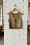 Brown sleeveless top on a wooden hanger against a white brick wall.