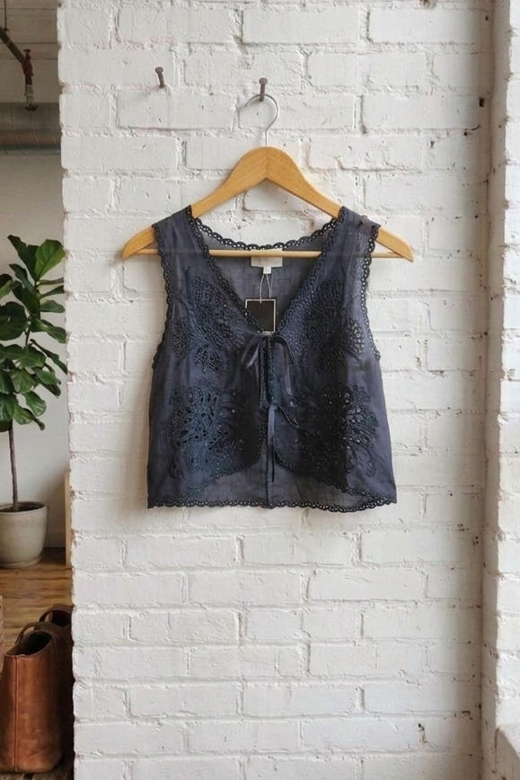 navy lace top on a wooden hanger against a white brick wall.