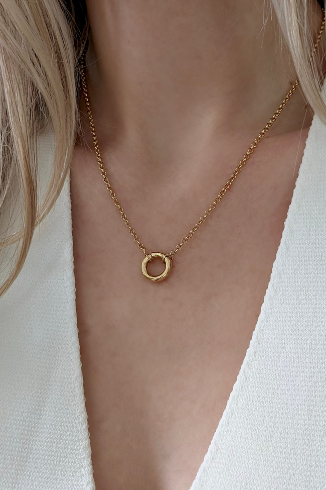 Gold necklace with a small circular pendant on a person wearing a white top.