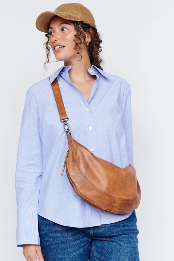 Woman wearing a light blue shirt, brown cap, and carrying a brown leather bag on a white background