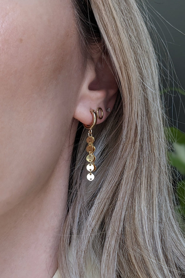 Close-up of a person wearing gold earrings with a blurred background
