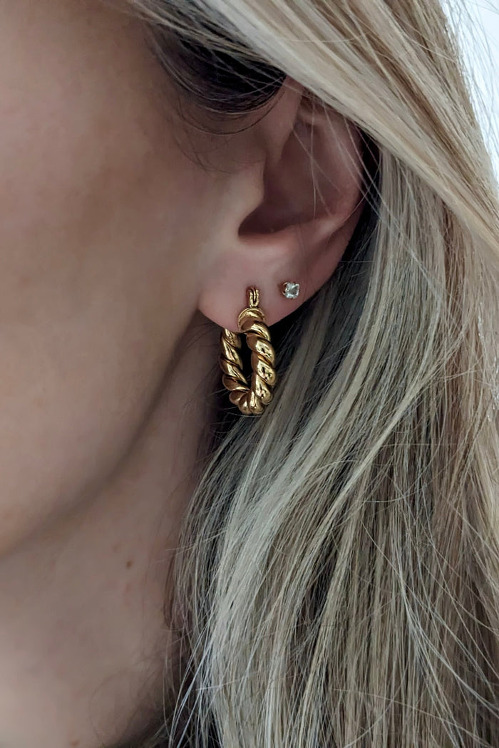 Close-up of a person wearing gold hoop earrings with a neutral background