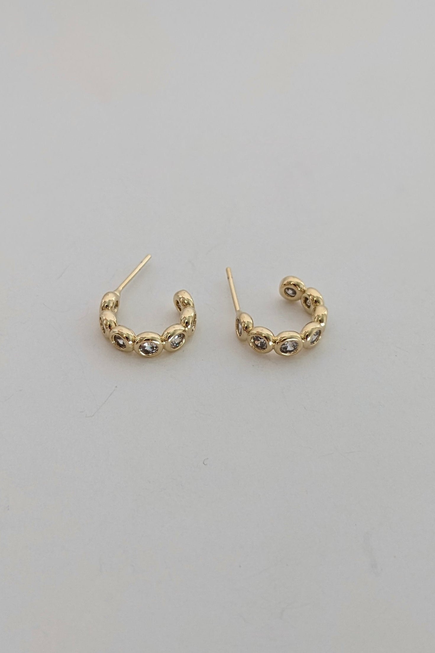 A pair of small gold sparkle hoop earrings with textured, beaded detailing along the front, displayed on a plain light gray surface.