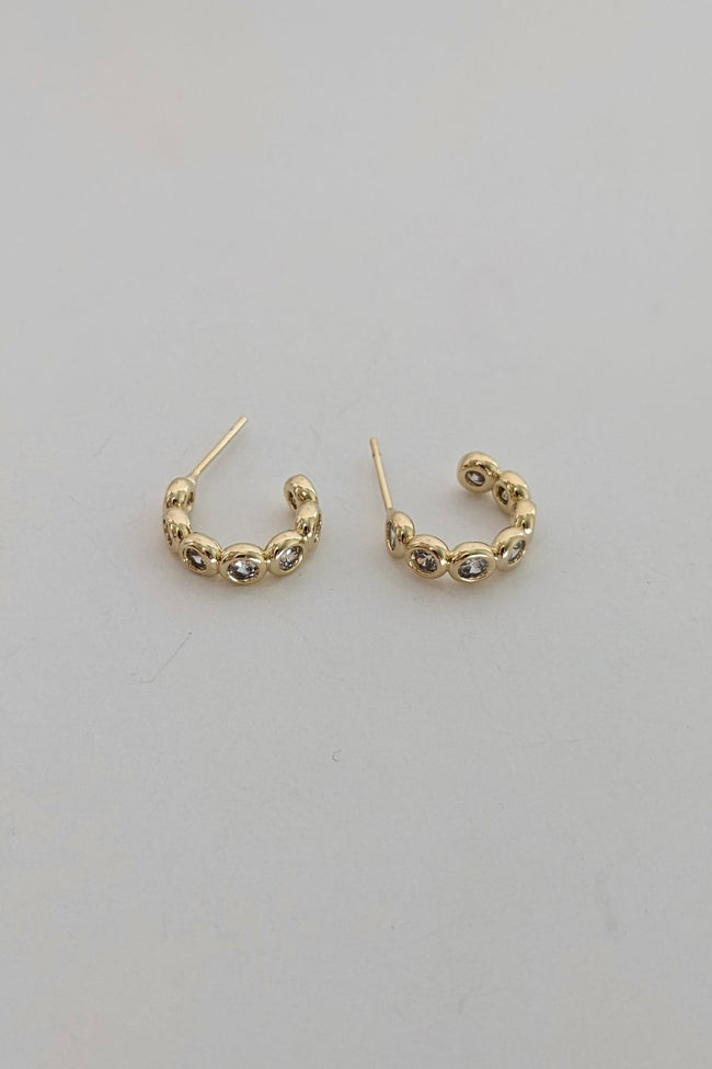 A pair of small gold sparkle hoop earrings with textured, beaded detailing along the front, displayed on a plain light gray surface.