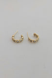 A pair of small gold sparkle hoop earrings with textured, beaded detailing along the front, displayed on a plain light gray surface.