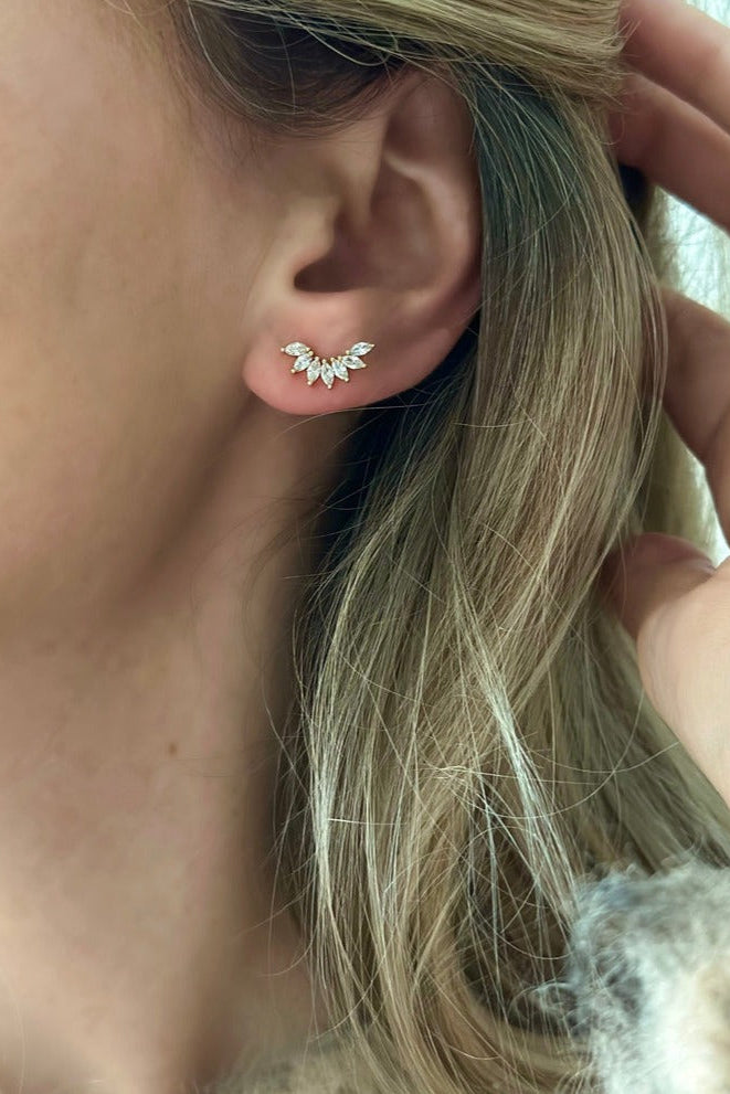 A person wearing gold-filled ear climbers adorned with cubic zirconium stones on their ear.