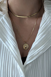 A person wearing a white shirt layered with a gold-filled chain necklace with a starburst pendant and a black cubic zirconia stone.
