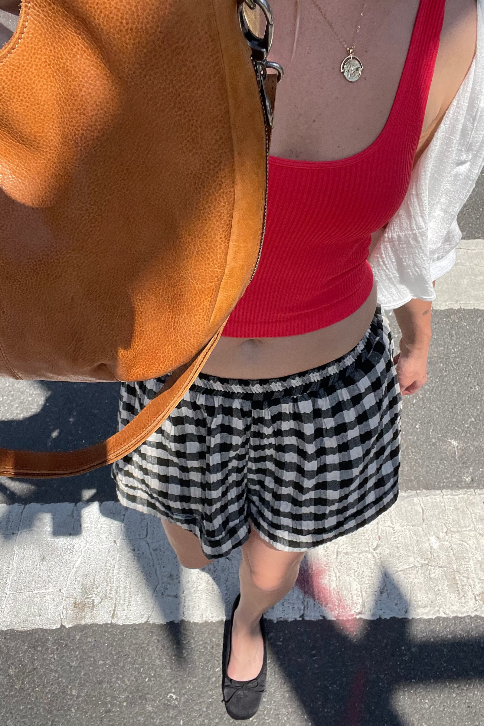 Person wearing a red top, black and white checkered skirt, and carrying a brown bag on a zebra crossing.