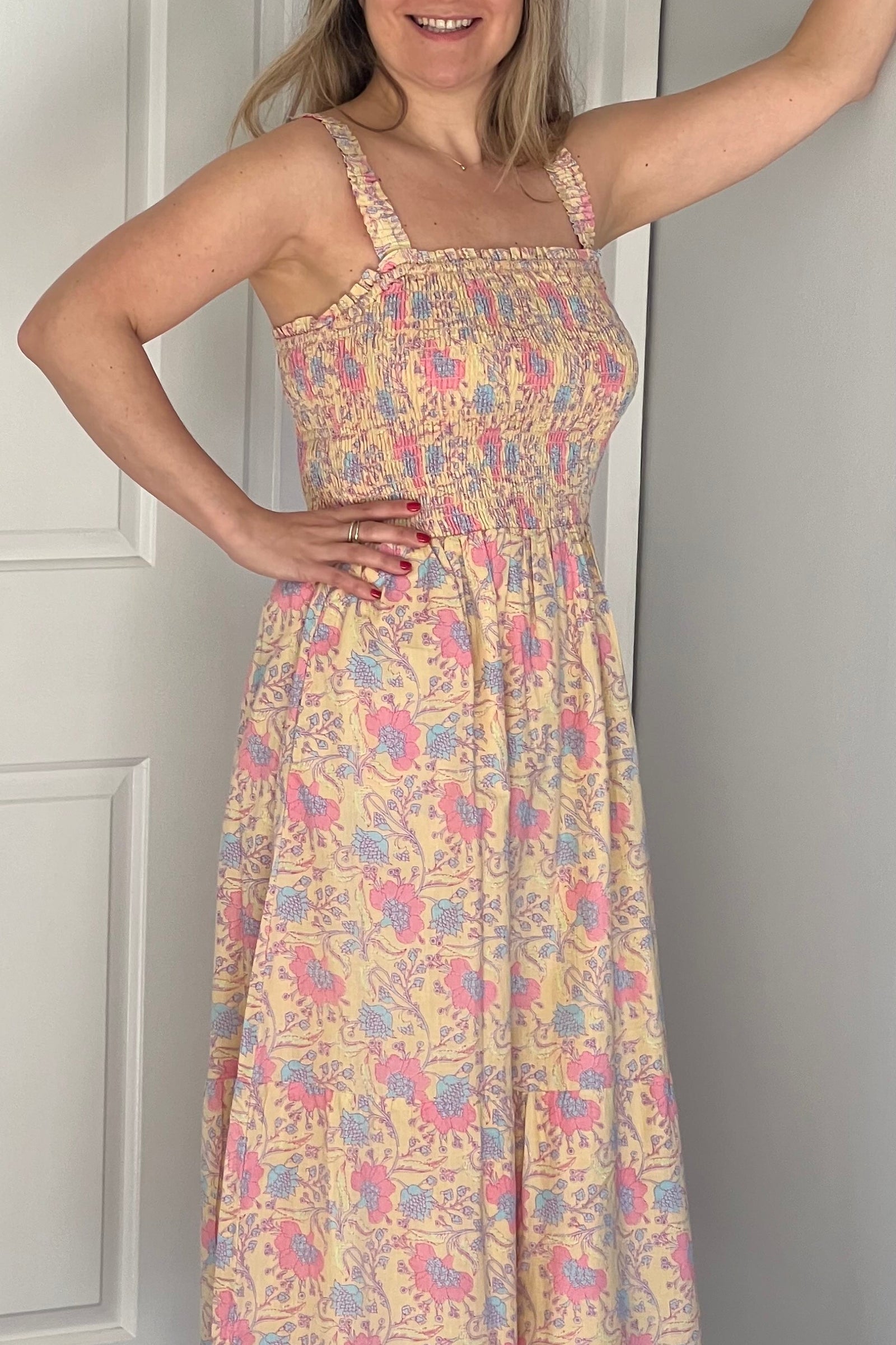 Woman wearing a floral dress standing in a room with white walls and a door.