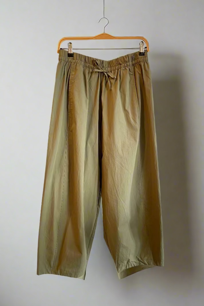 Green pants hanging on a wooden hanger against a white wall.