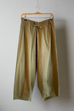 Green pants hanging on a wooden hanger against a white wall.