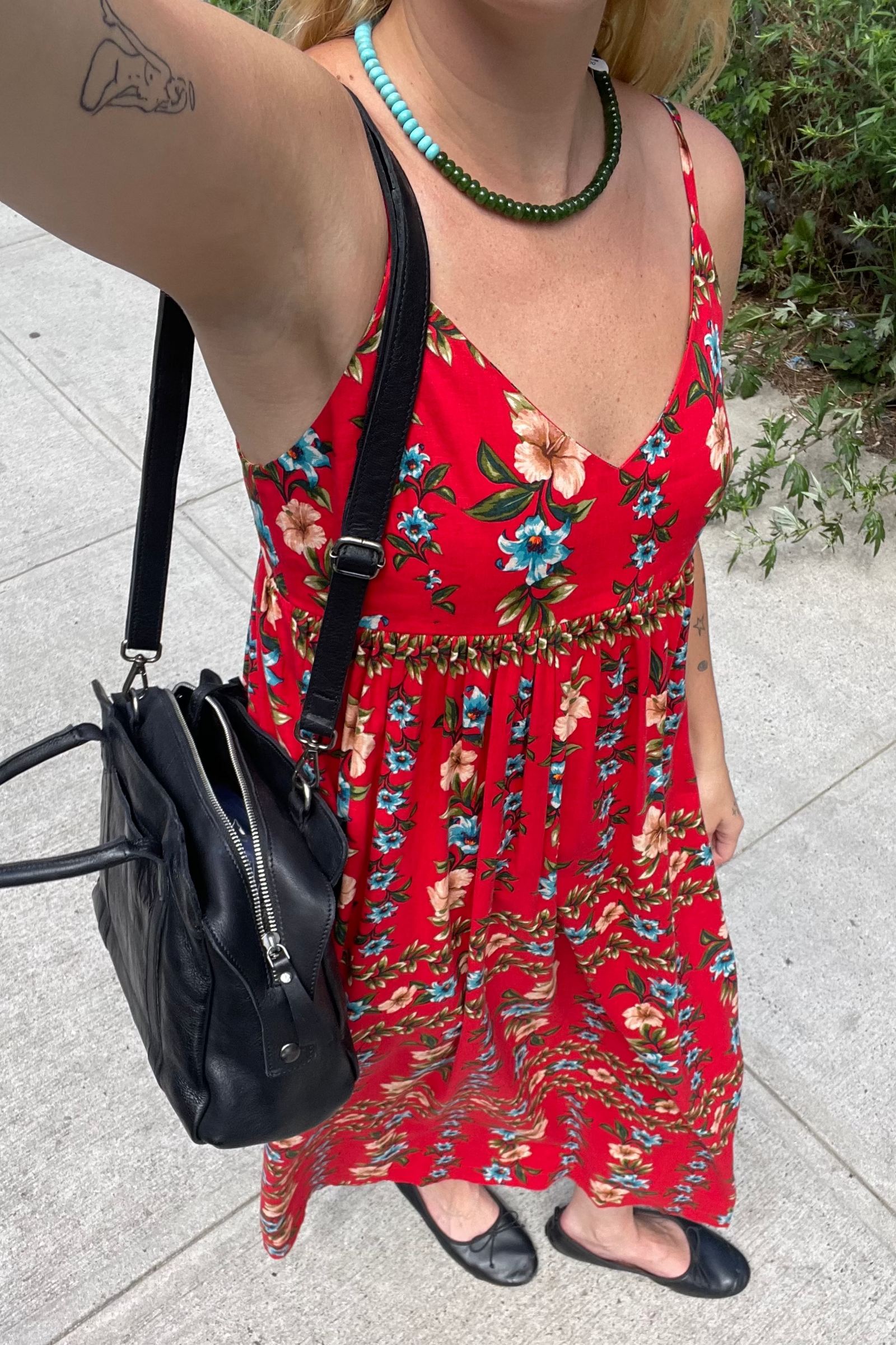 Person wearing a red floral dress holding a black bag on a sidewalk.