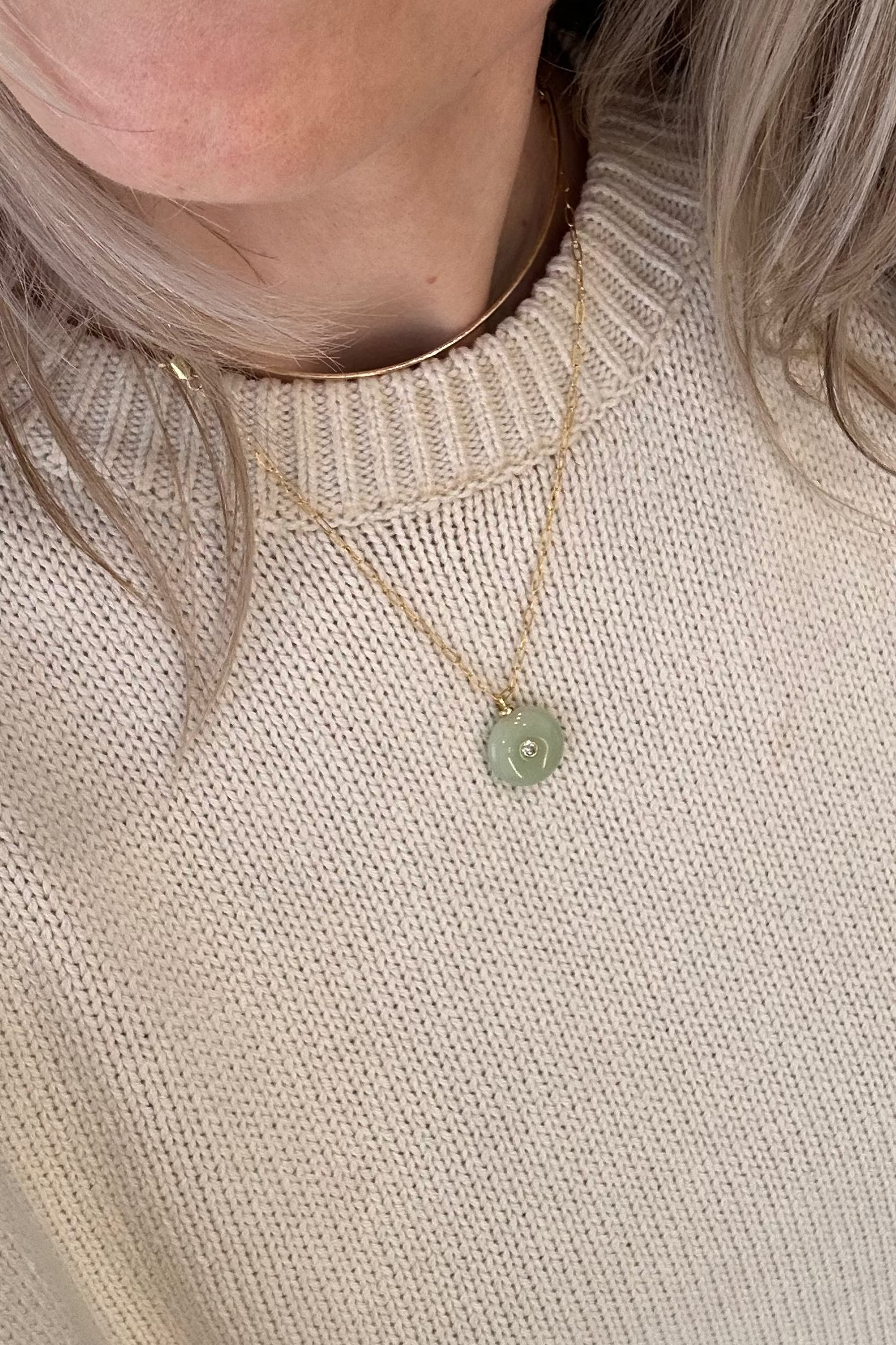 Close-up of a person wearing a gold necklace with a green pendant.