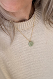 Close-up of a person wearing a gold necklace with a green pendant.