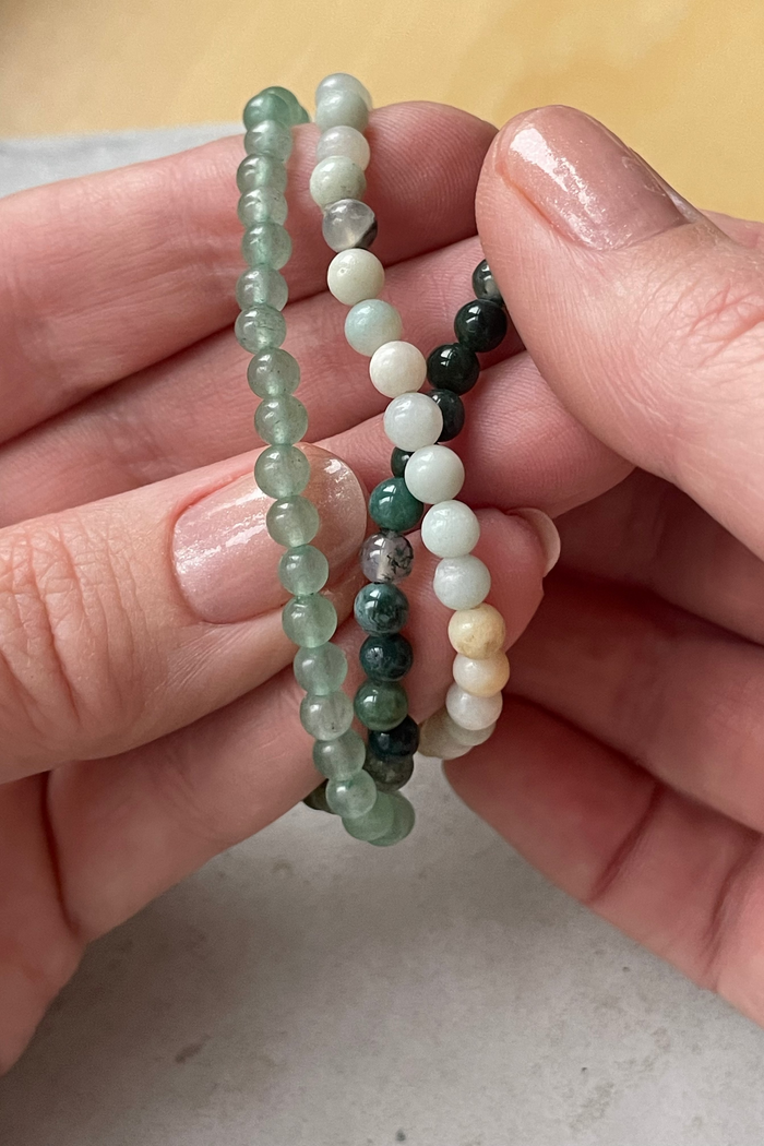 Three beaded bracelets of different colors held between fingers on a neutral background