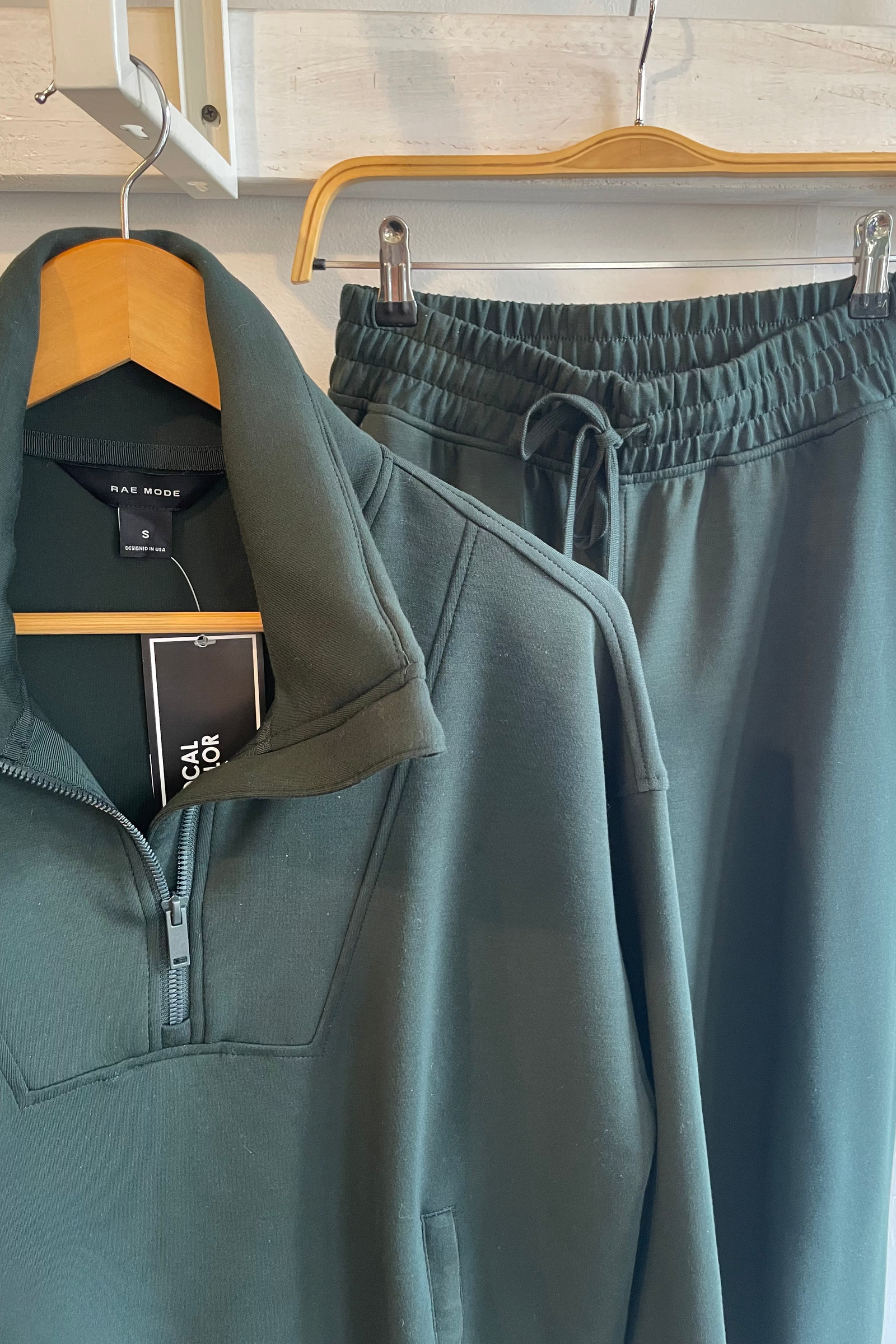 Green half-zip sweatshirt and pants on hangers with tags attached.