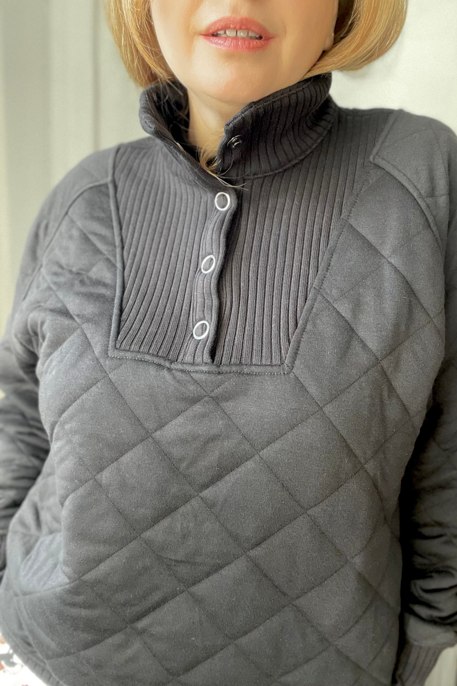 Person wearing a black quilted pullover with a white background