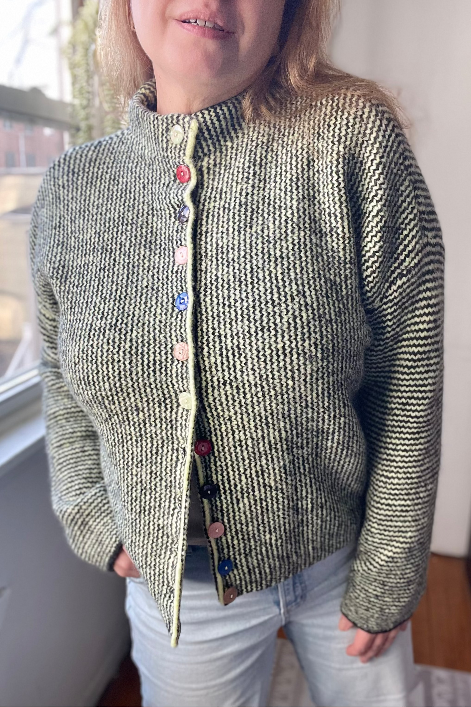 Person wearing a textured green cardigan with colorful buttons indoors.