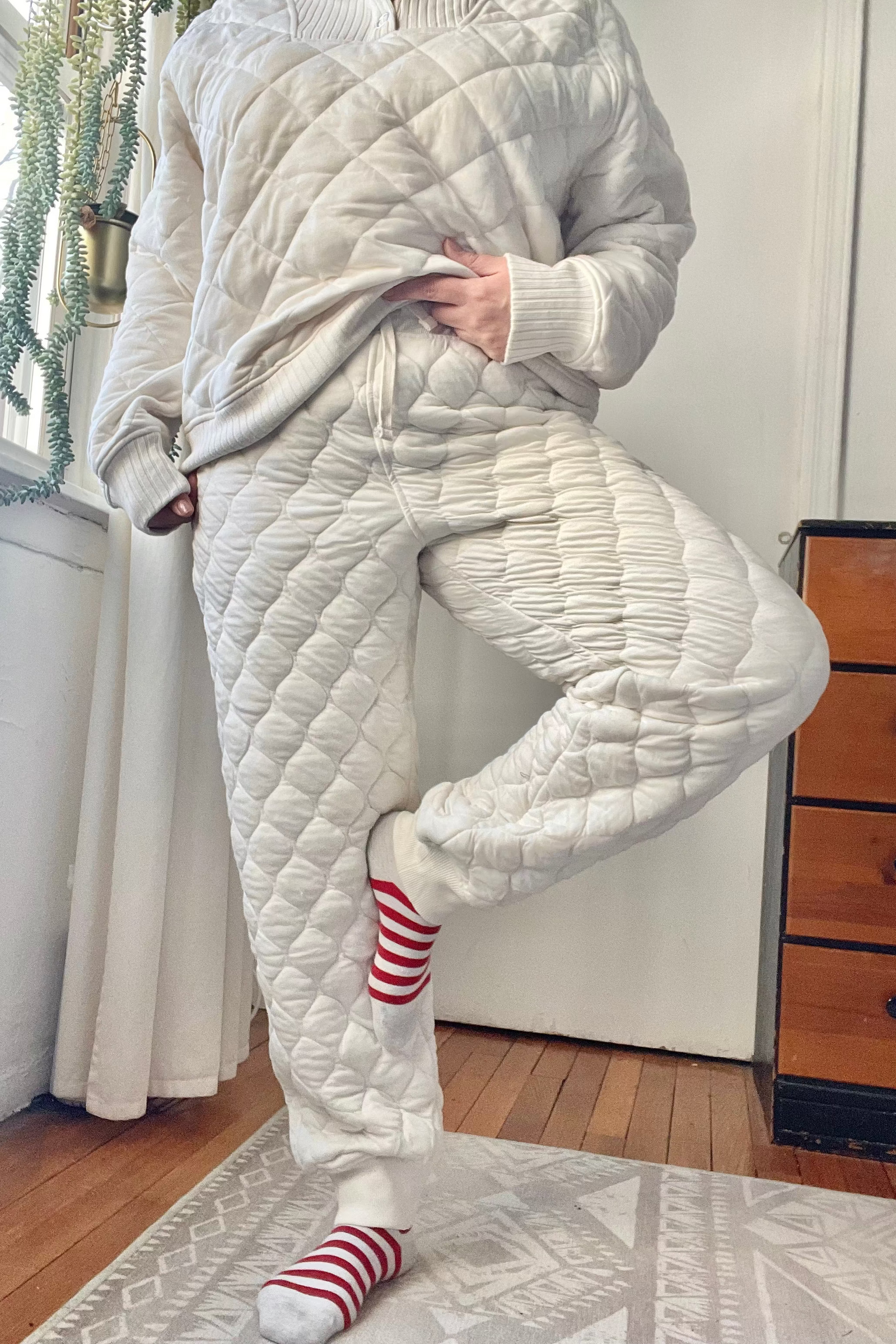 Person wearing a quilted white outfit in a room with wooden floors and a dresser.