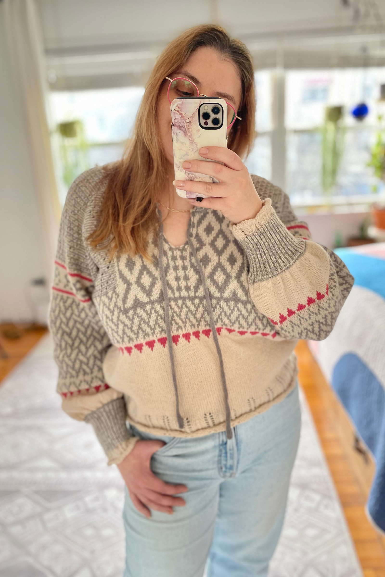 Person wearing a patterned sweater taking a mirror selfie in a room.