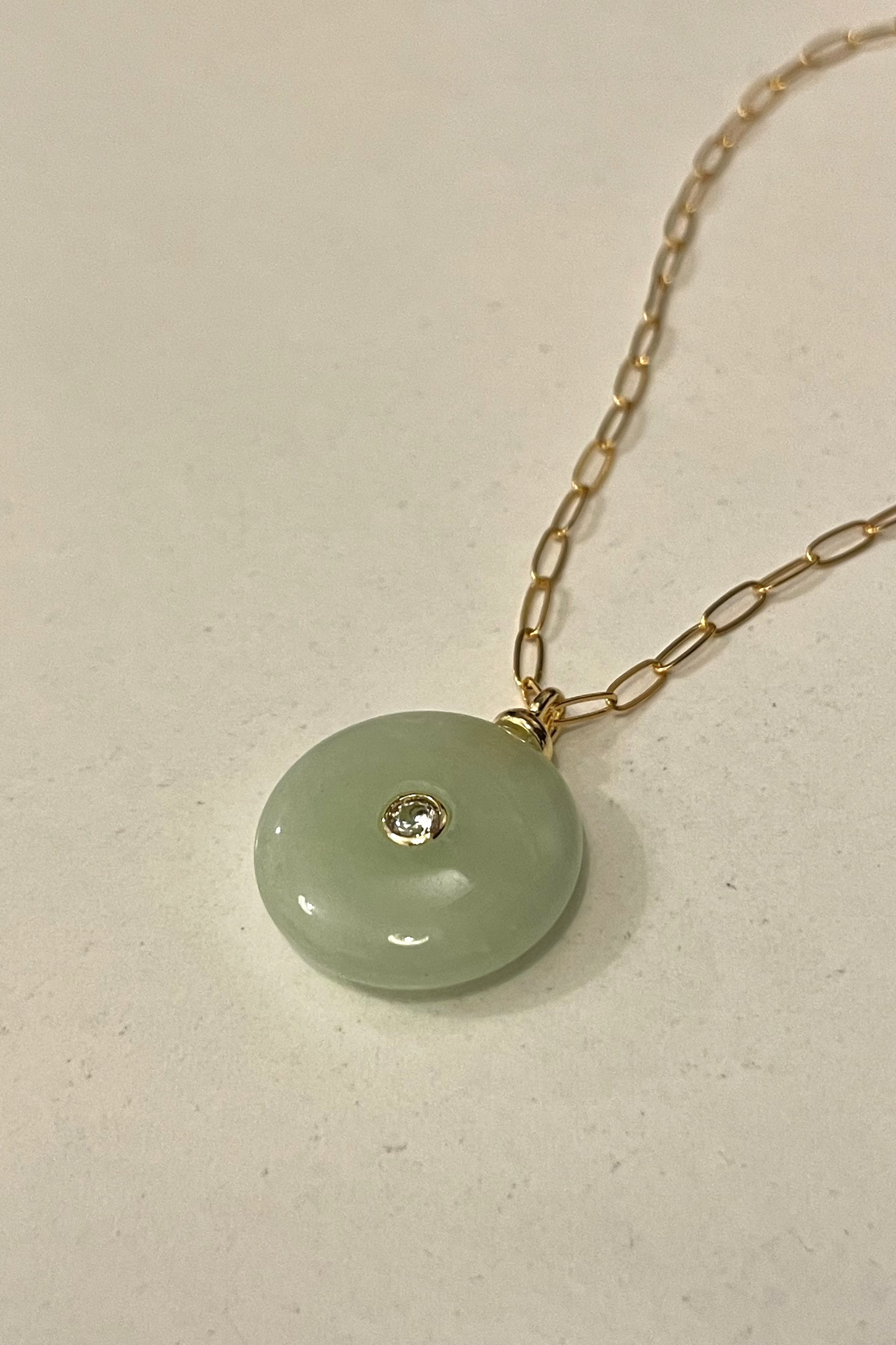 Necklace with a green pendant and gold chain on a light background