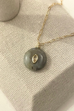 Necklace with a gray pendant and gold chain on a textured beige surface