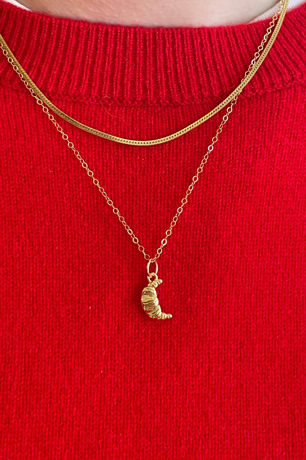 Gold necklace with a small croissant pendant on a red sweater