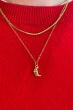 Gold necklace with a small croissant pendant on a red sweater
