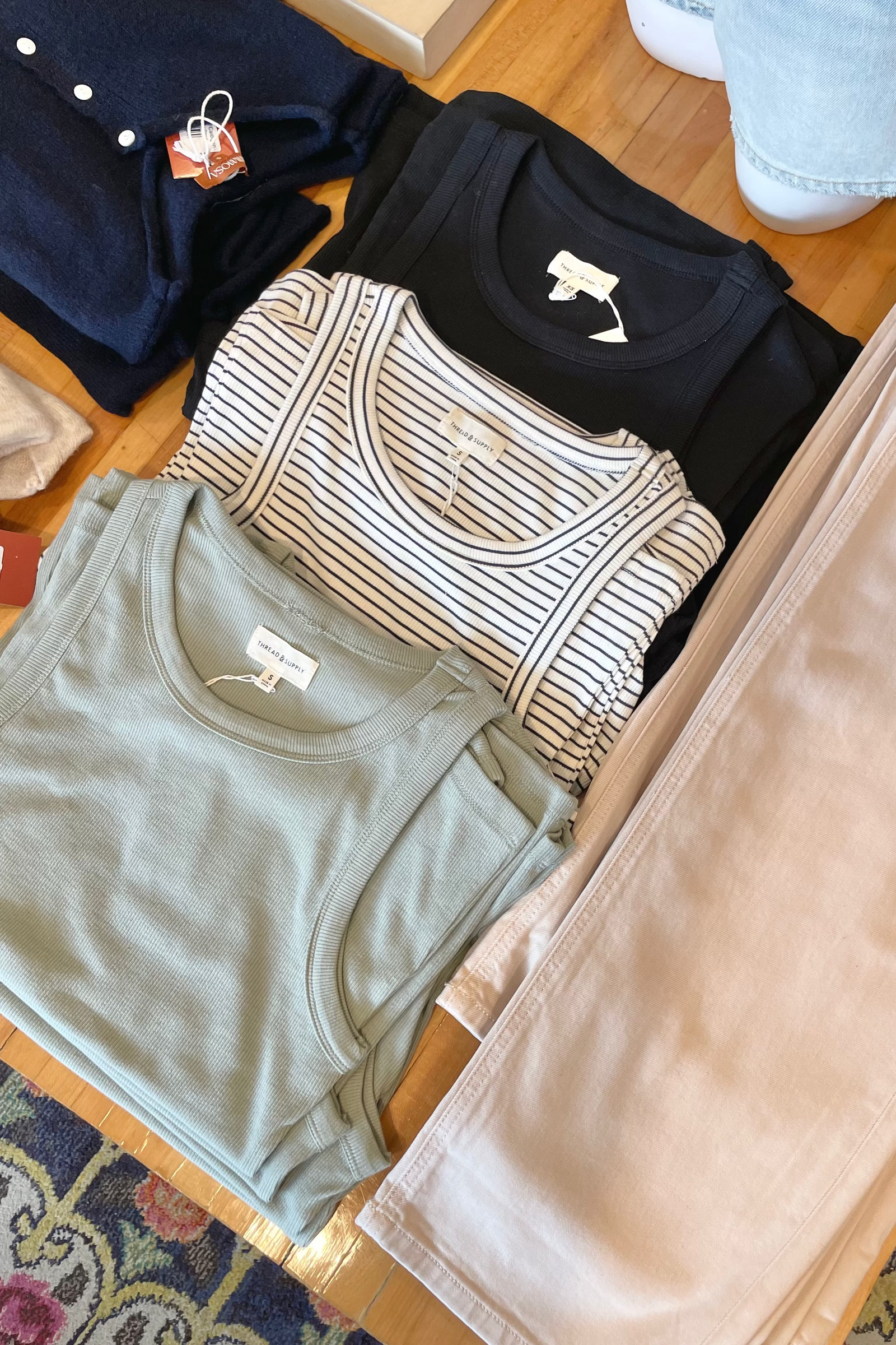 Folded clothes including a green shirt, striped shirt, and beige pants on a wooden surface.