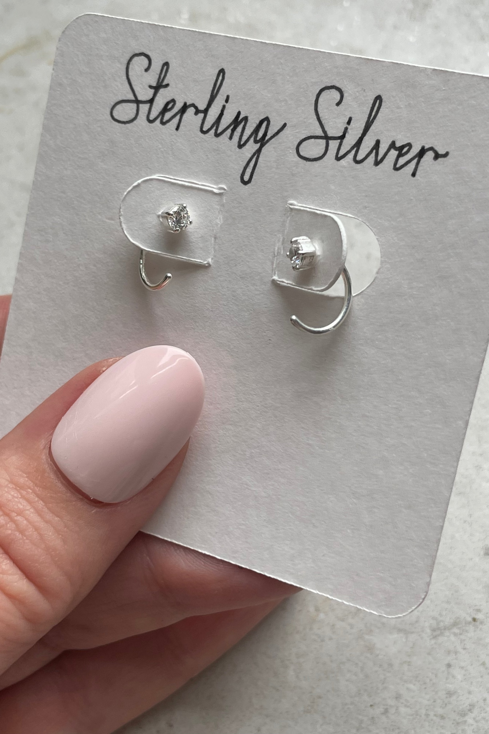  silver 3/4 huggie earrings on a card with 'Sterling Silver' text, held by a hand.