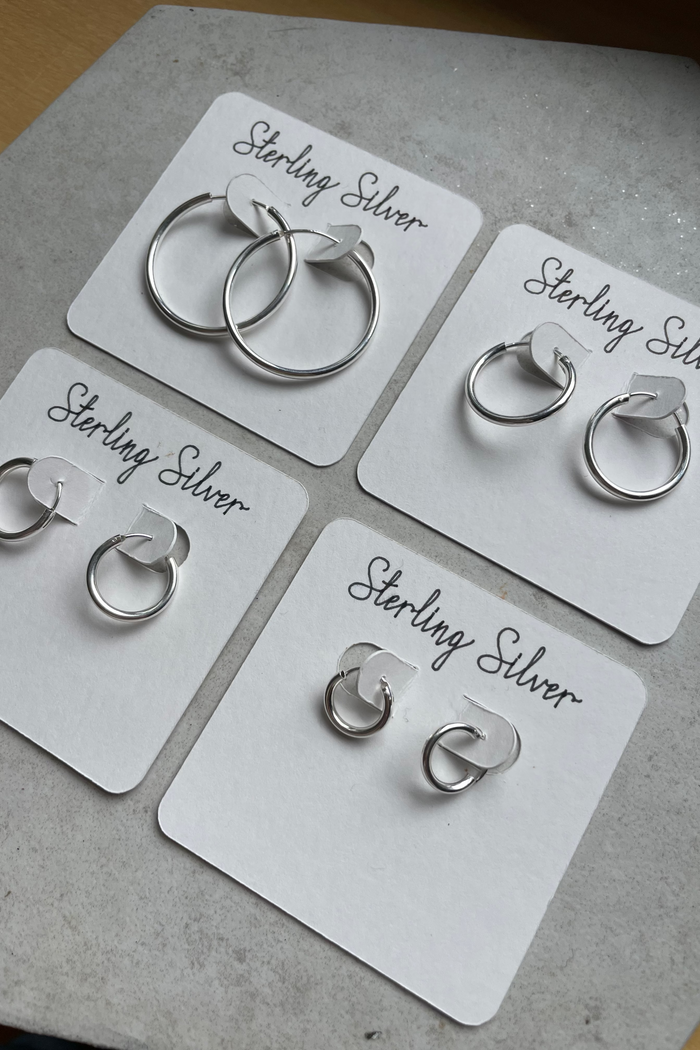 Set of silver earrings on white cards labeled 'Sterling Silver' on a gray surface.