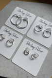 Set of silver earrings on white cards labeled 'Sterling Silver' on a gray surface.