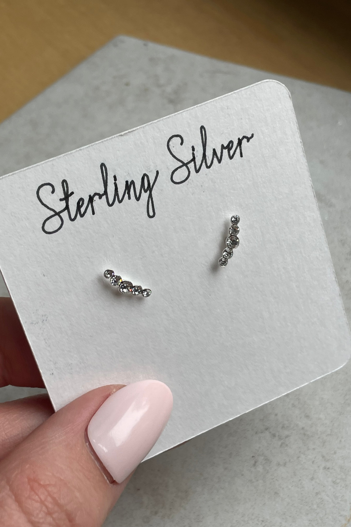 Pair of silver earrings on a 'Sterling Silver' card held by a hand with pink nail polish.