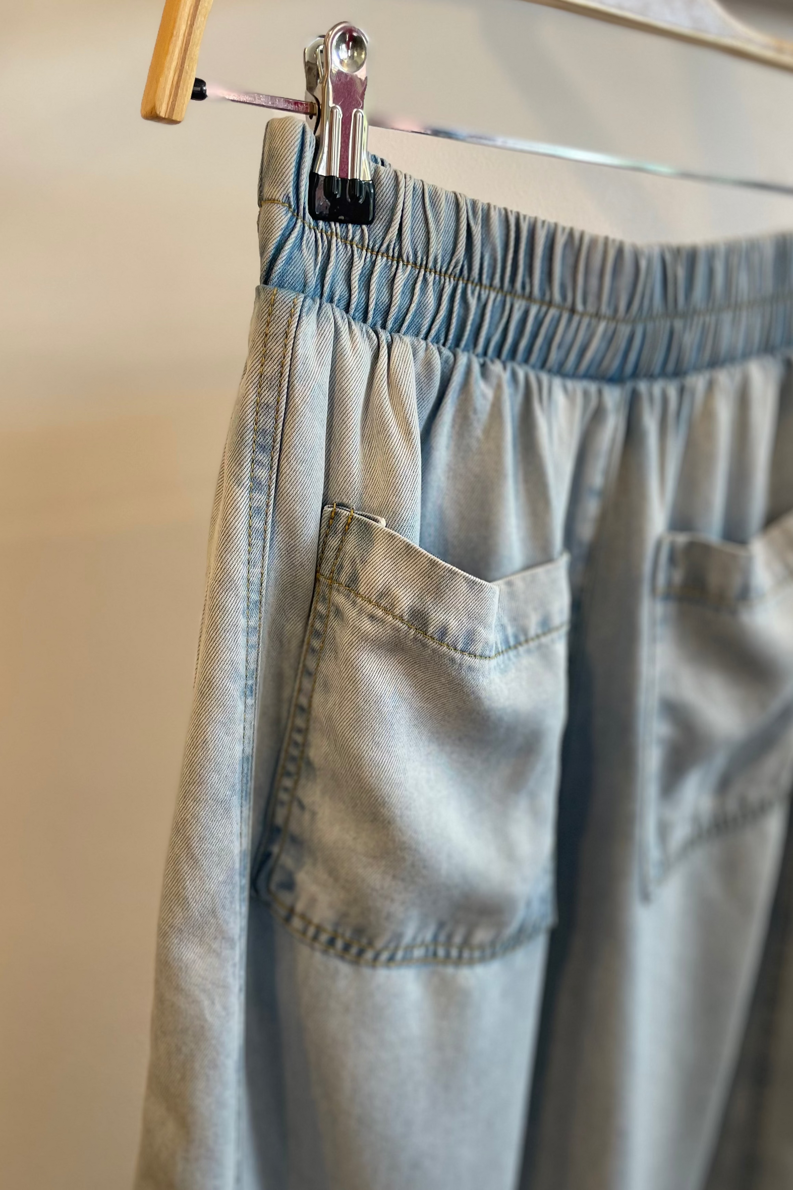 Light blue pants hanging on a rack against a neutral background