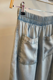 Light blue pants hanging on a rack against a neutral background