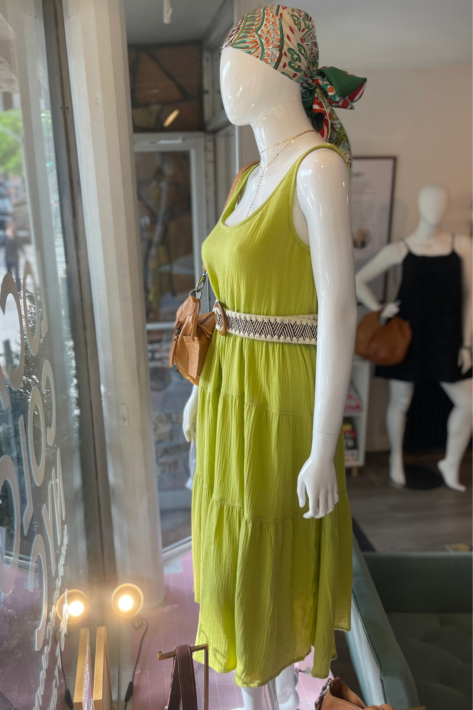 Mannequin wearing a green dress with a patterned headscarf in a store window.