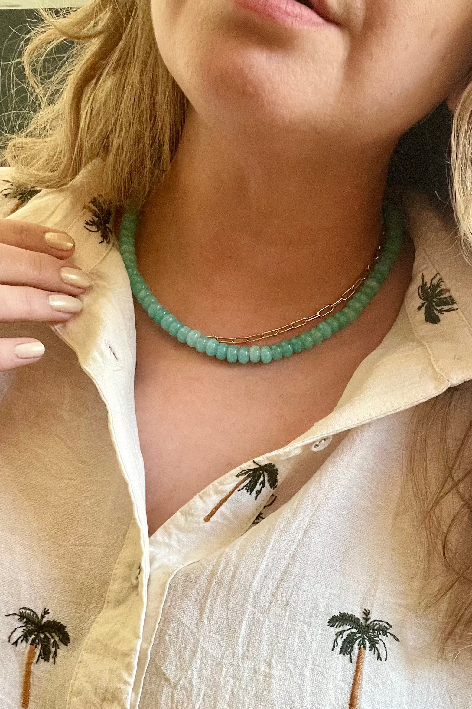 Close-up of a person wearing a white shirt with palm tree designs and a green beaded necklace.