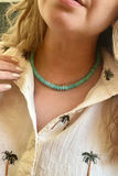 Close-up of a person wearing a white shirt with palm tree designs and a green beaded necklace.
