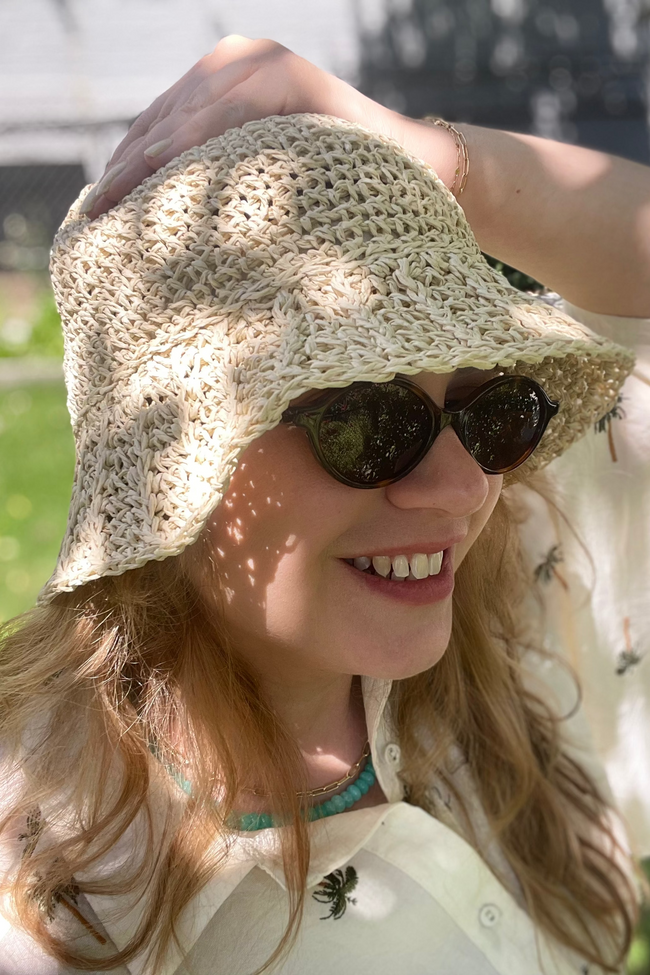 Woman wearing a beige crochet hat and sunglasses outdoors
