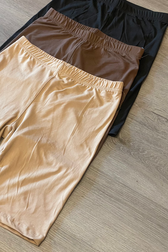 Three pairs of shorts in black, brown, and beige on a wooden floor.