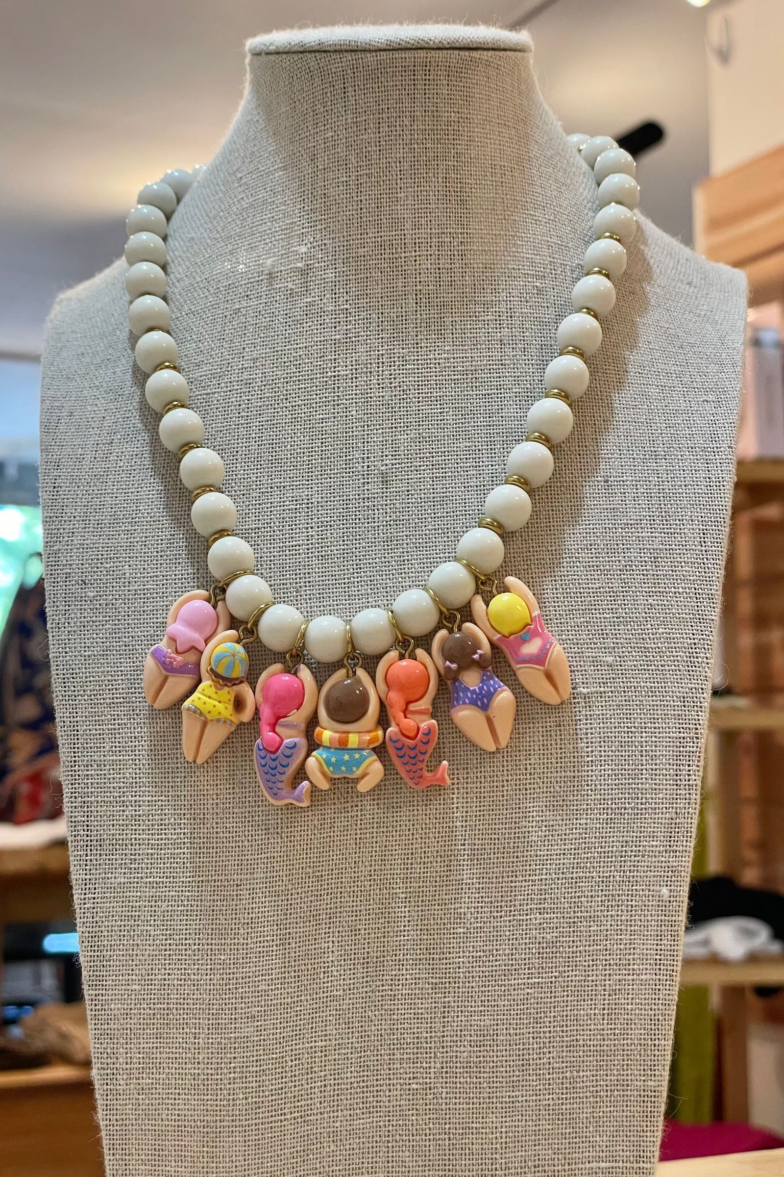 Necklace with white beads and colorful mermaid-themed charms on a mannequin bust.