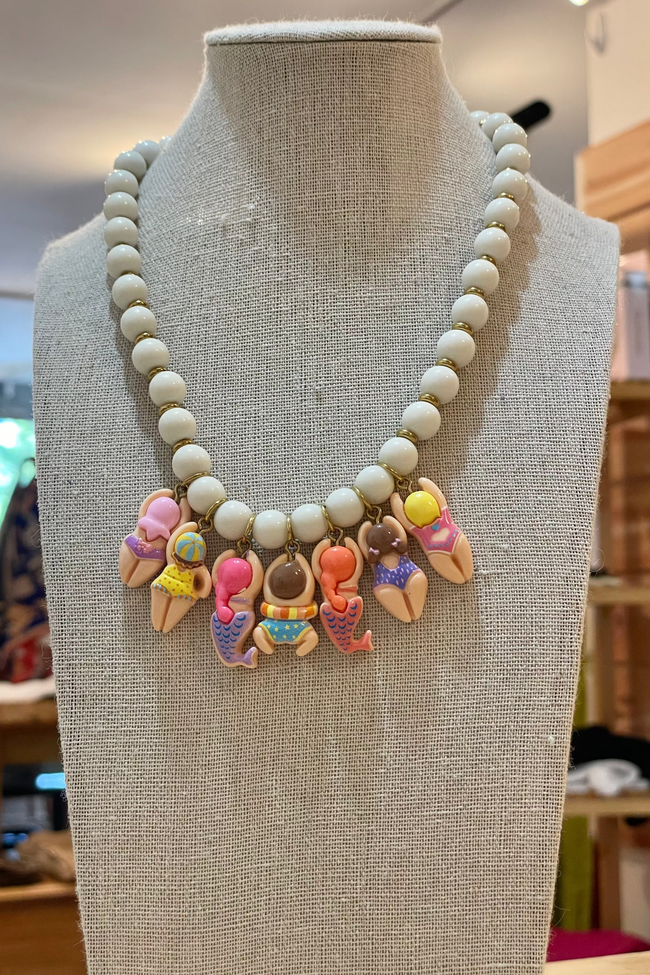 Necklace with white beads and colorful mermaid-themed charms on a mannequin bust.