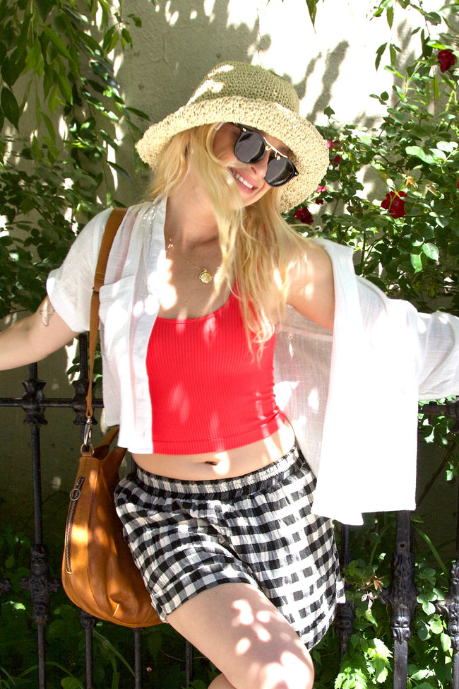 Woman in a red top and checkered shorts standing against a leafy background