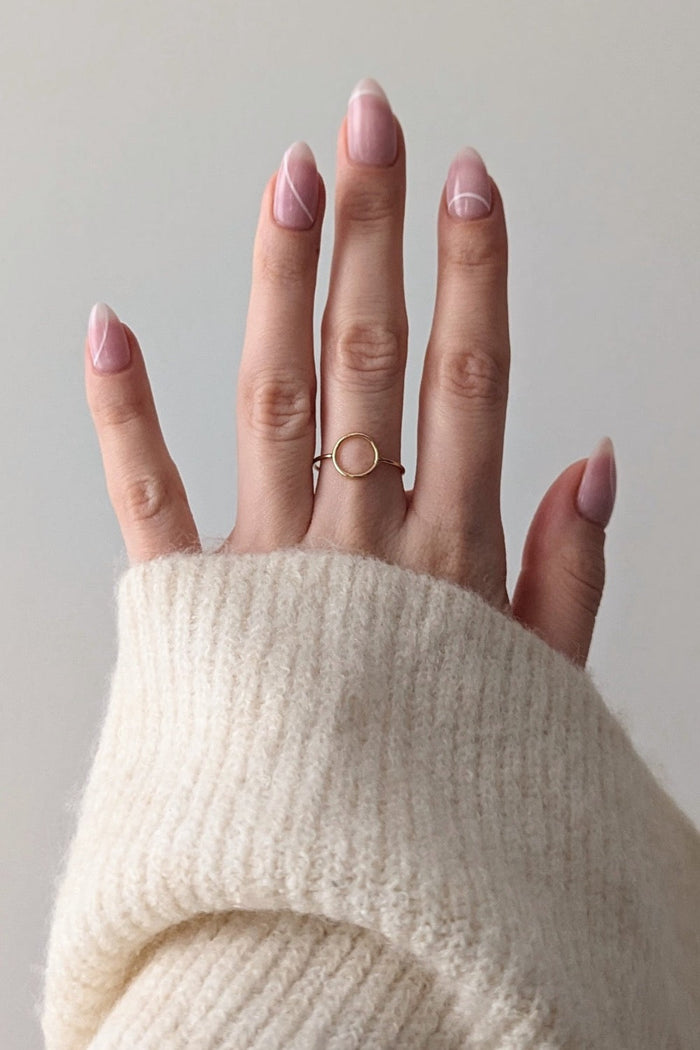 A person's hand wearing a gold filled circle ring, with the ring visible on the finger.