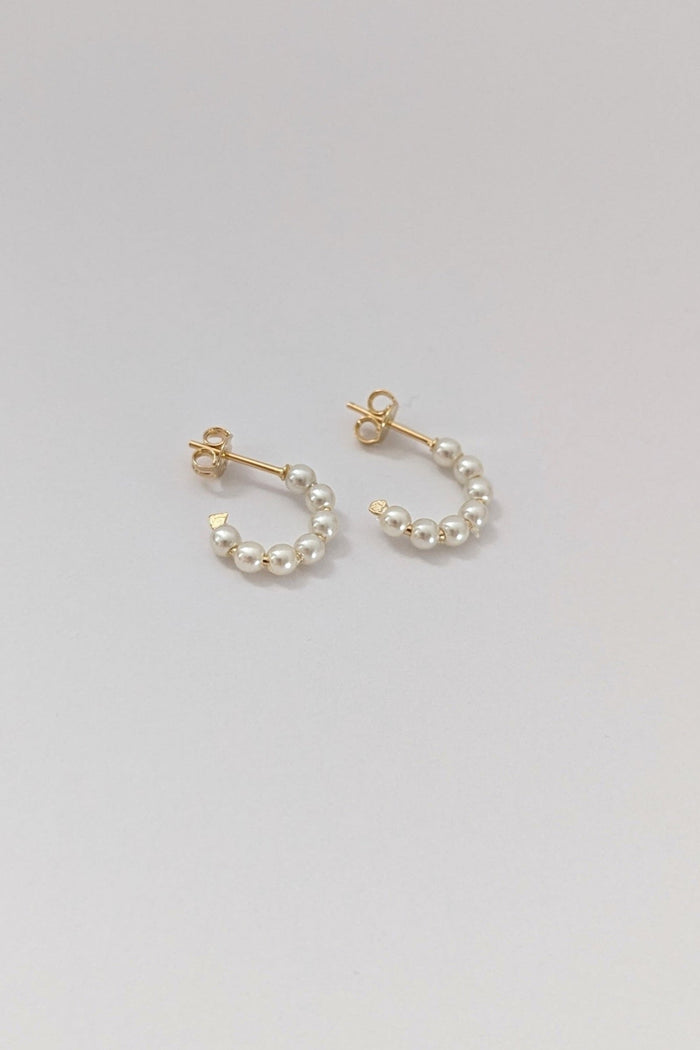A pair of gold-colored mini pearl hoop earrings on a white background.