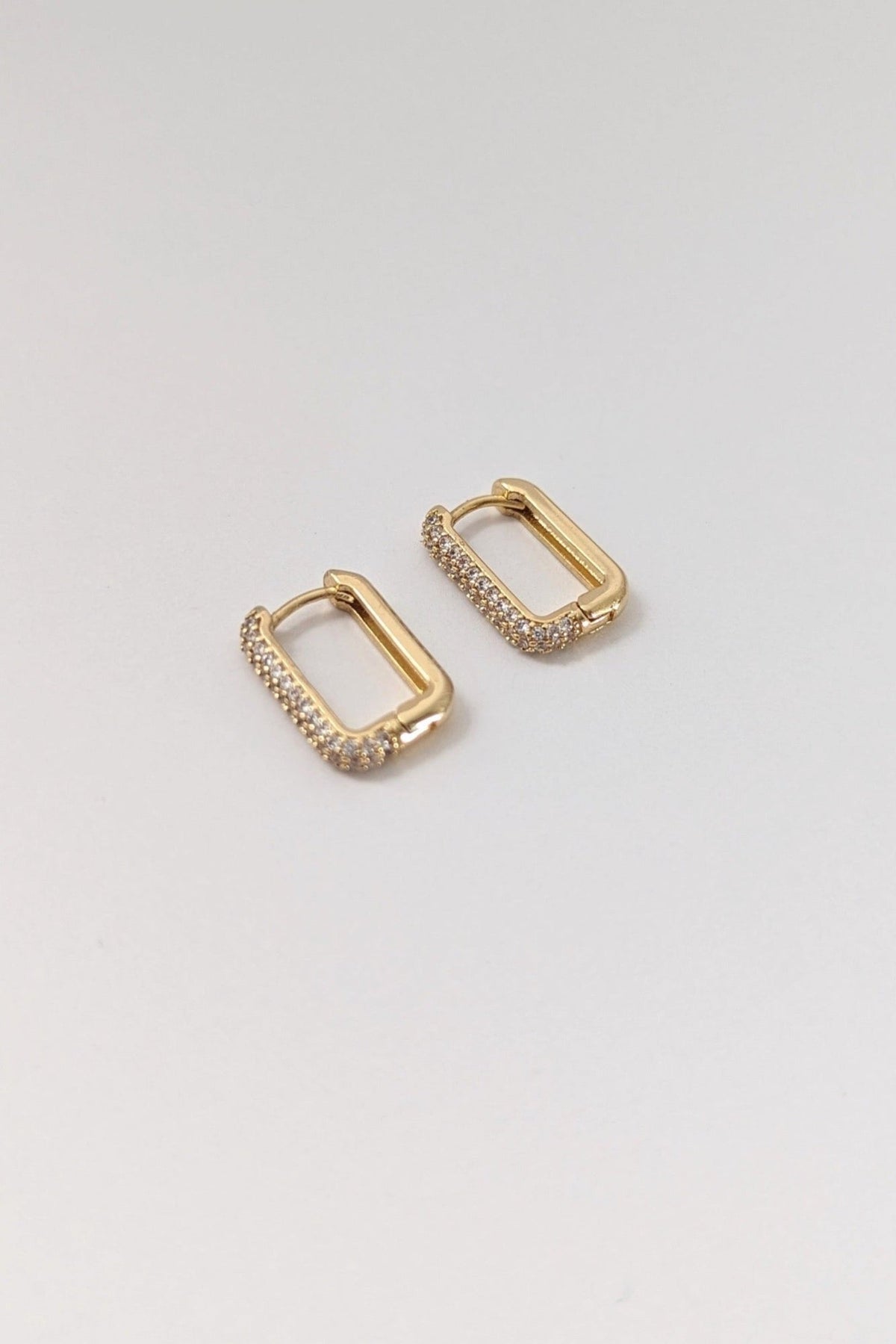 A pair of gold-colored rectangular pave huggie earrings on a white background