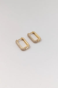 A pair of gold-colored rectangular pave huggie earrings on a white background